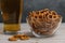 Glass of beer and salty mini pretzels in a deep glass bowl on a wooden tabletop