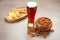 Glass of beer served with delicious pretzel crackers and other snacks on grey table