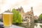 Glass of beer with view of historic houses, canal and belfry tower in city center in Bruges