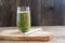 A glass of bleached celery, banana and basil smoothie next to a reusable bamboo straw on a wooden stand against a background of