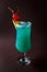 Glass of blue coctail with cherry and slice of pineapple on elegant dark brown background