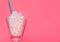 Glass with blue straw filled with sugar cubes on pink background. Junk food concept.