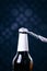 Glass bottle of beer and opener on a dark background. Hand opening a bottle. Alcohol and drinks concept.