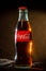 Glass bottle of Coca-Cola on a dark background, light reflections on the edges of the glass; Belarus, Minsk, July 26, 2019.