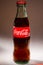 Glass bottle of Coca-Cola on a light background, light reflections on the edges of the glass; Belarus, Minsk, July 26, 2019.