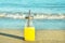 Glass Bottle with Freshly Pressed Tropical Fruits Juice with Straw Standing on Beach Sand. Blue Turquoise Foamy Sea Waves