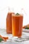 A glass and a bottle of freshly squeezed carrot juice with greens with straws on a white background