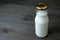 Glass Bottle full of milk isolated on dark colored wooden table with copy space