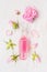 Glass bottle of pink rose water on white wooden background with bud and petal