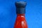 Glass bottle with red sauce with black cork on blue background