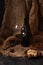 Glass and bottle of red wine with cheese, raisins, and nuts on sackcloth, dark background