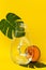 Glass bottle with tropical plants and honeydew melon. Summer refreshments with fruit and monstera plant leaf on yelllow background