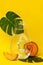 Glass bottle with tropical plants and honeydew melon. Summer refreshments with fruit and monstera plant leaf on yelllow background