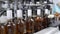 Glass bottles filled with prune tincture move along conveyor line with control panel in modern distillery for bottling