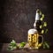 Glass bottles and mug of beer with cap of foam and hops on table at dark rustic background, front view, Still life