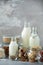 Glass bottles of vegan plant milk and almonds, nuts, coconut, hemp seed milk on grey concrete background. Banner with copy space.