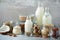 Glass bottles of vegan plant milk and almonds, nuts, coconut, hemp seed milk on grey concrete background. Banner with copy space.