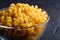 Glass bowl with cavatappi uncooked golden wheat curly pasta on textured dark black background