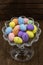 Glass bowl with colorful Easter eggs from sloping top with dark wood background to Easter