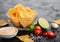 Glass bowl plate with potato crisps chips with paprika flavour on black stone table background. Red and green chilli peppers with