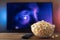 A glass bowl of popcorn and remote control in the background the TV works. Evening cozy watching a movie or TV series at