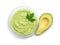 Glass bowl of tasty guacamole with parsley and cut avocado on white, top view
