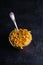 Glass bowl and vintage spoon with cavatappi uncooked golden wheat curly pasta on textured dark black background