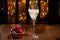 Glass of brut champagne bubbles wine in tulip glass and bowl with fresh strawberries on evening bar lights background