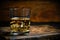 Glass chilled whiskey with ice cubes on wooden background in cellar