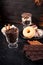 Glass with coffee beans next to chocolate tablets, donuts, brown sugar and other glass with peanuts in chocolate