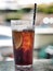 Glass of cola with ice cube, slice of lemon and straw in glass