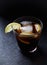 Glass of cola with lemon and ice cubes. Dark stone background.