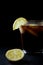 Glass of cola with lemon and ice cubes. Dark stone background.
