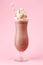 Glass of cold chocolate milkshake with whipped cream on pink background