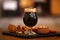 Glass of cold tasty dark beer served with snack on table