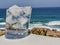 Glass of cold water with ice cubes against rocks and the blue sea.