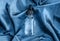 Glass cosmetics dropper bottle on smooth blue silk or satin folds closeup. Cloth texture background. Abstract wallpaper