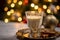 Glass of creamy eggnog with nutmeg, Christmas tree and wrapped gifts blurred in the backdrop.