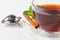 A glass cup with black tea on a saucer with mint, cinnamon and lemon, and a tea strainer.