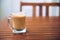 Glass or cup of coffee with white foam on brown wooden table on the balcony, with wooden chair in the background, with copy space