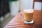 Glass or cup of coffee with white foam on brown wooden table on the balcony, with wooden chair in the background, with copy space