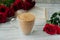 Glass Cup with hot coffee, whipped foam and sprinkled with cinnamon with red bouquet of roses and book on the background