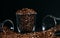 A glass cup overflowing with brown roasted coffee beans. Lots of coffee beans in the foreground with glass cups on both