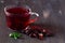 Glass cup of red hibiscus hot tea with dry flowers rose with fresh green leaves of mint on a dark wooden background.