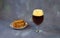 Glass of dark beer with foam and a plate with wheat croutons on a gray abstract background