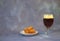A glass of dark beer with white foam, next to a plate with wheat croutons