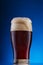 Glass of dark craft beer with foam on blue background