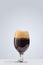 Glass of dark foamy beer isolated over gray background. Concept of alcohol drinks, party