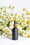 A glass dropper bottle of black color against a background of fragrant field daisies. Natural cosmetics and skin care. Aroma