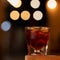 Glass of expensive alcoholic drink with ice cube. Cold strong beverage on black background with backlit bokeh. Copy